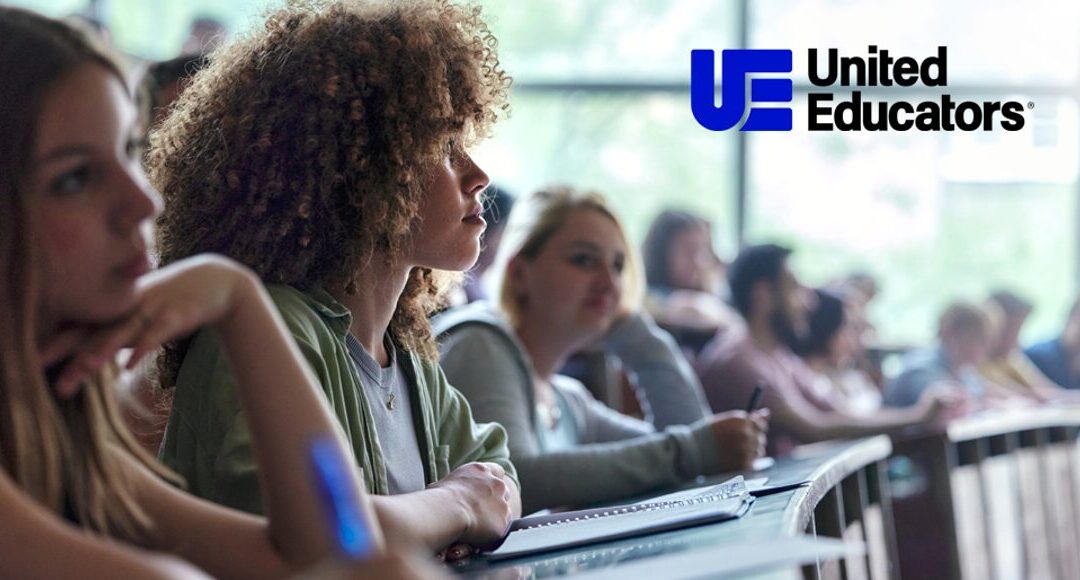 Young female student looking up to head of class, United Educators Logo in shot
